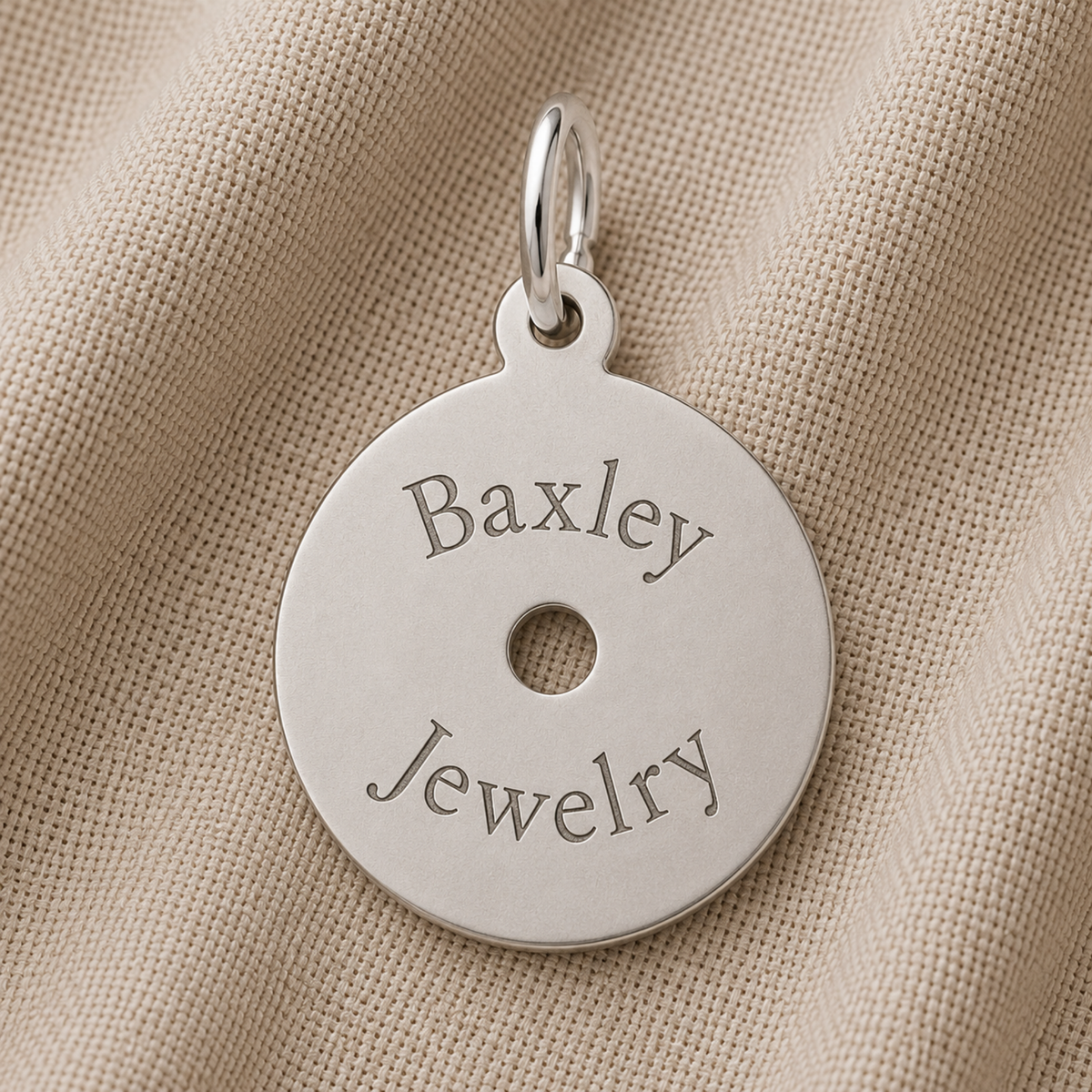A round sterling silver CD Charm by Rembrandt Charms, engraved with “Baxley Jewelry,” rests on beige textured fabric—a perfect necklace and thoughtful gift for any music lover.