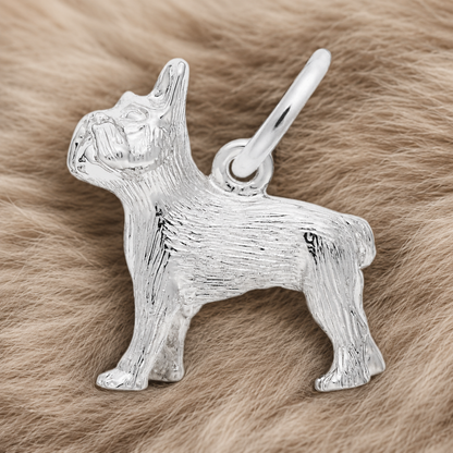 A gold-plated French Bulldog-shaped charm from Rembrandt Charms rests on a soft, beige, fur-like surface, making for an adorable French Bulldog keepsake.