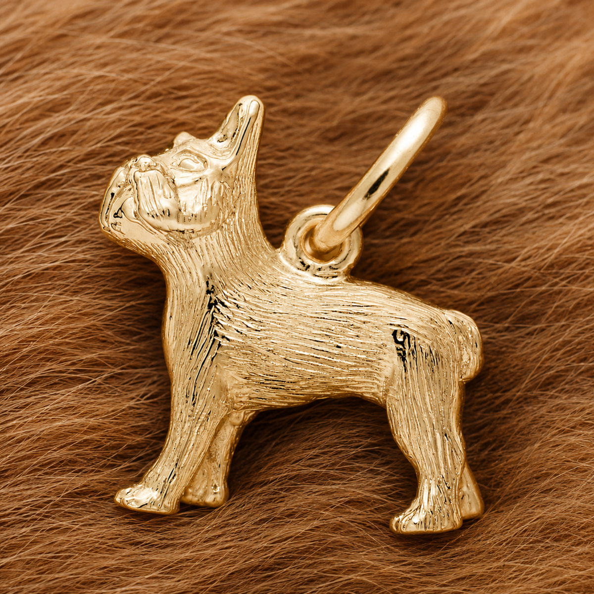 A French Bulldog Dog Charm—gold plated by Rembrandt Charms—rests atop a soft, brown, fur-like surface, making an elegant pet keepsake and a thoughtful gift for any dog lover.