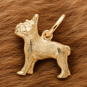 A French Bulldog Dog Charm—gold plated by Rembrandt Charms—rests atop a soft, brown, fur-like surface, making an elegant pet keepsake and a thoughtful gift for any dog lover.