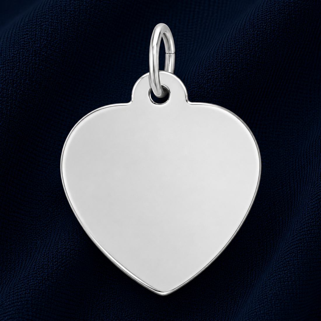 A gold-plated Medium Heart – 35 Series Charm by Rembrandt Charms, featuring a sleek heart shape with a small loop at the top and displayed on a dark blue textured fabric background—ideal as an engravable jewelry piece or a meaningful personalized gift.