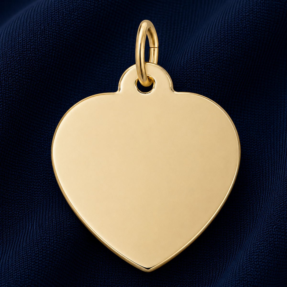 A Rembrandt Charms Medium Heart – 35 Series Charm in gold plate, featuring a smooth, unengraved surface—ideal as engravable jewelry or a meaningful personalized gift—displayed against dark blue textured fabric.