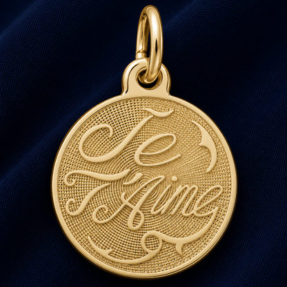 A round sterling silver pendant from Rembrandt Charms, engraved with the words “Je t’aime,” rests on a dark blue fabric background, making this elegant Je T’aime Disc Charm a timeless piece of romantic jewelry.