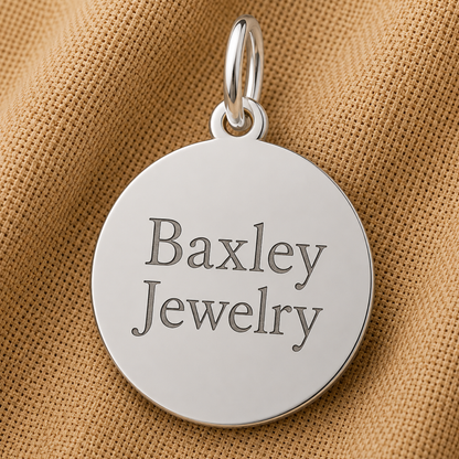 A round sterling silver “Je T’aime Disc Charm” by Rembrandt Charms rests on a textured tan fabric background, evoking the timeless elegance of romantic jewelry reminiscent of a French love charm.