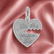 The Heart and Key charm by Rembrandt Charms, crafted in sterling silver and featuring a heart-shaped pendant with a jagged keyhole and the engraved message “THE KEY THAT FITS UNLOCKS MY HEART,” is elegantly displayed on pink satin fabric—making it the perfect piece of romantic jewelry and an unforgettable anniversary gift.