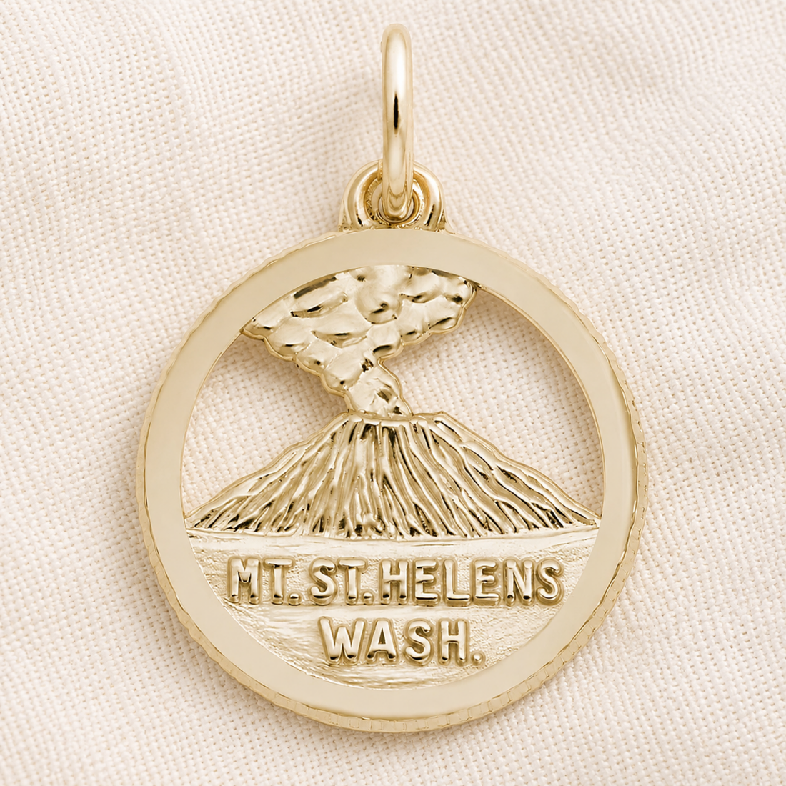 The Rembrandt Charms Mount St. Helens Disc Charm in sterling silver features an engraved depiction of the Mt. St. Helens volcano emitting smoke, with “MT. ST. HELENS WASH.” inscribed below—an eye-catching piece of volcano jewelry and the perfect Pacific Northwest keepsake, beautifully photographed on a light fabric background.