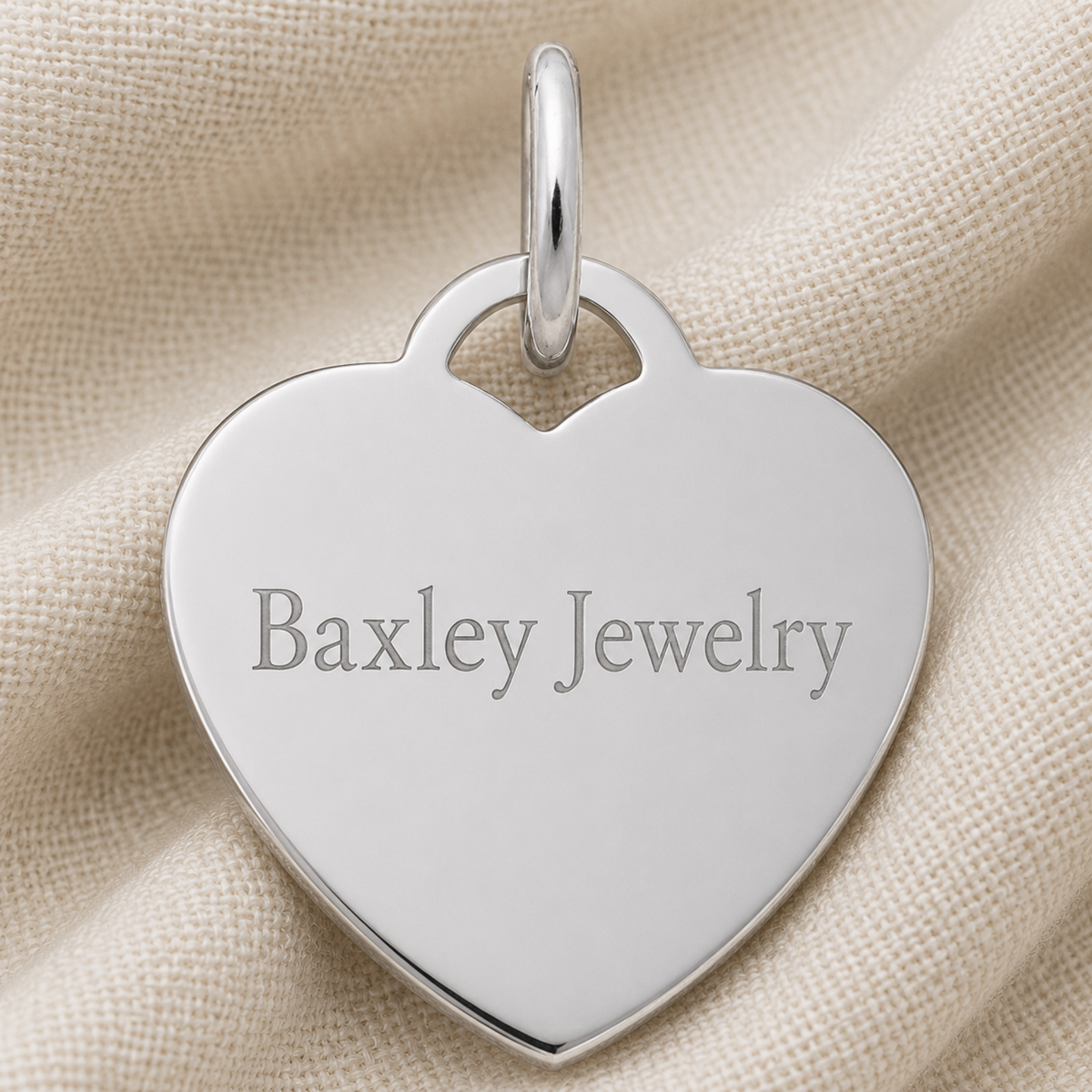 A Large Heart Classic Series Charm in sterling silver from Rembrandt Charms, perfect for personalized jewelry, rests on beige textured fabric.
