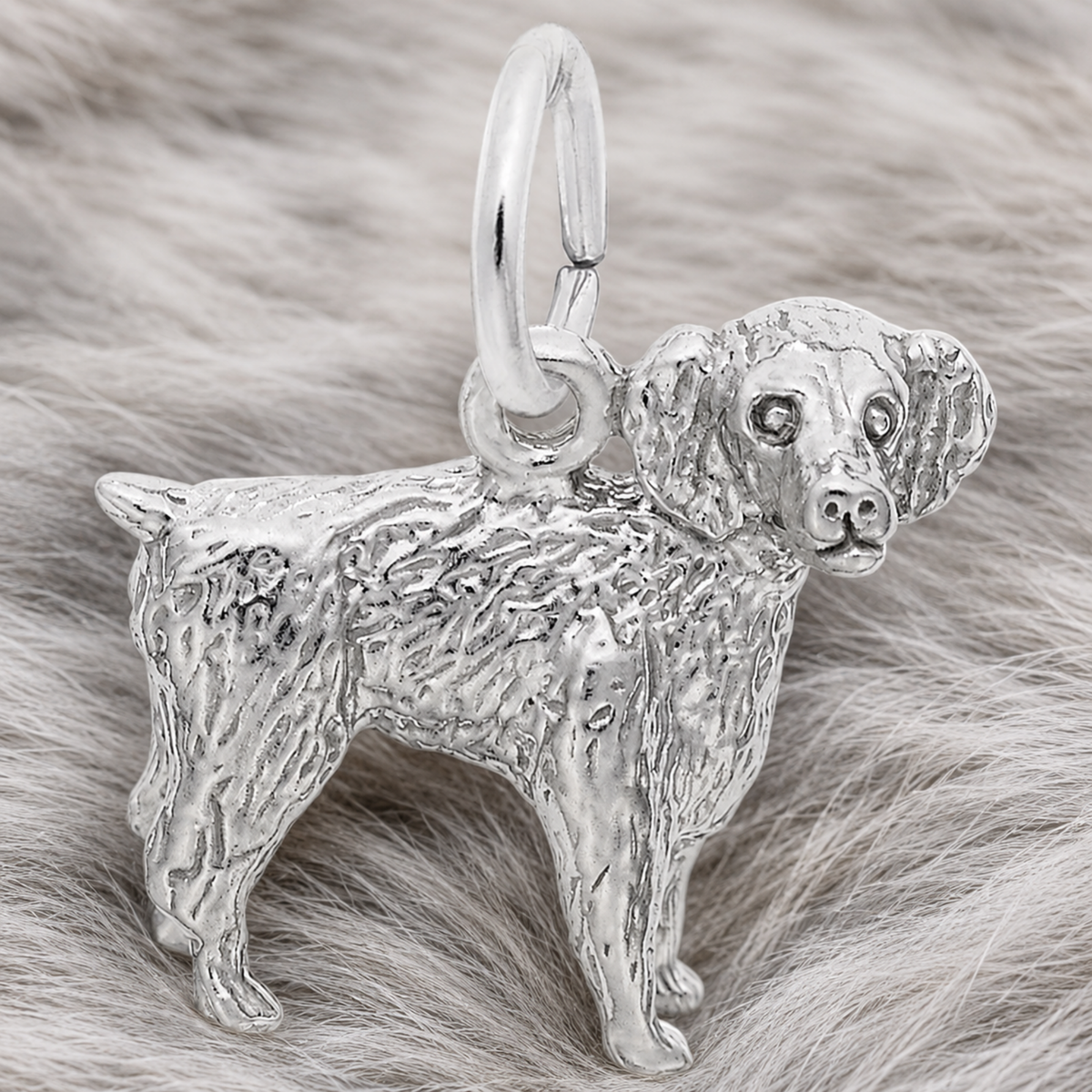 A gold-plated Boykin Spaniel Charm by Rembrandt Charms, featuring detailed fur texture and displayed on a soft, light gray fur background—a perfect jewelry piece for dog lovers inspired by South Carolina’s beloved state dog.