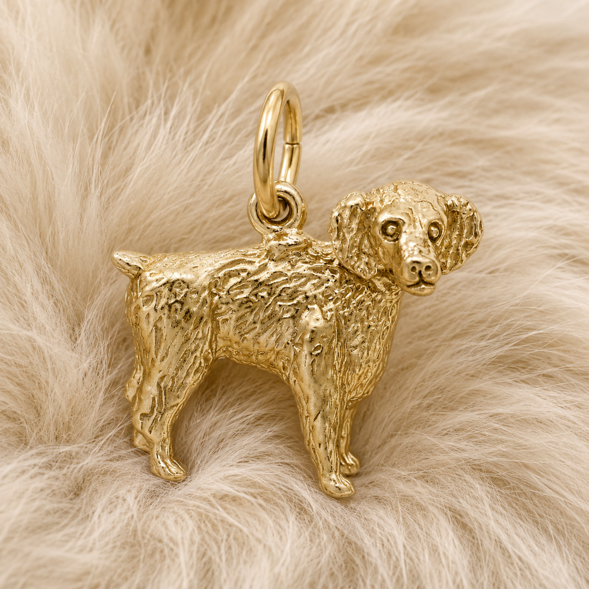 The Boykin Spaniel Charm—Gold Plated by Rembrandt Charms, inspired by South Carolina’s beloved state dog and detailed with curly fur, rests on a soft, light beige, fluffy surface—making it a perfect addition to any dog lover’s jewelry collection.