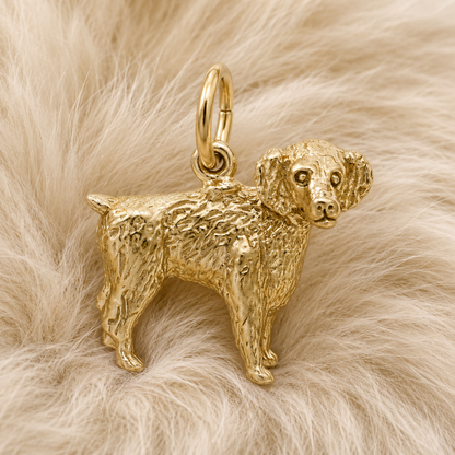 The Boykin Spaniel Charm—Gold Plated by Rembrandt Charms, inspired by South Carolina’s beloved state dog and detailed with curly fur, rests on a soft, light beige, fluffy surface—making it a perfect addition to any dog lover’s jewelry collection.