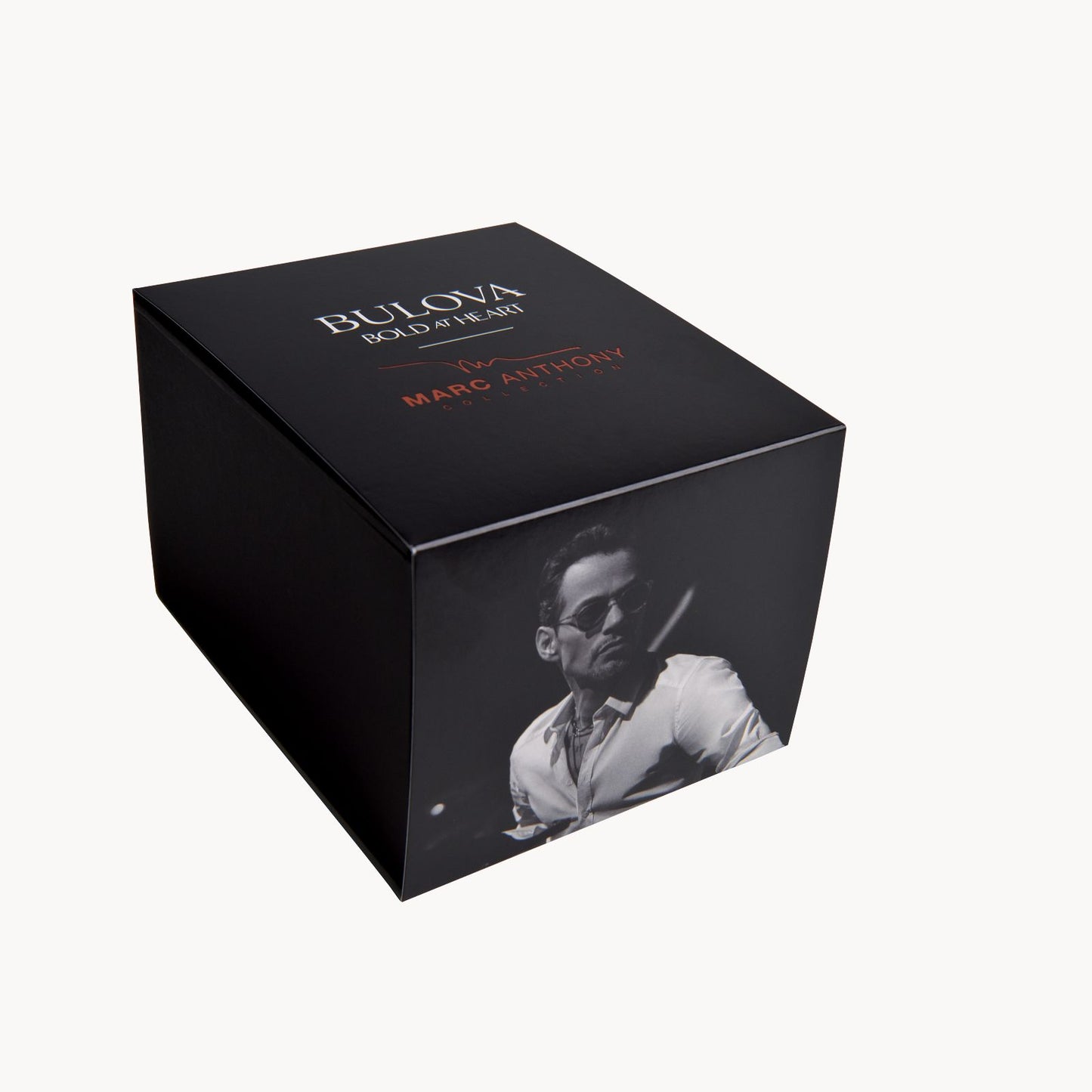 A black rectangular Bulova Watch Company box with “Bold at Heart” and “by Marc Anthony” on the lid, plus a grayscale man-in-sunglasses photo—perfect for gifting your Bulova Marc Anthony Marine Star White Dial Women's Watch.