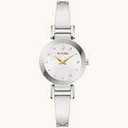 The Marc Anthony "Valió la Pena" Women's Watch with Diamonds by Bulova features a sleek silver design with a minimalist round dial accented by sparkling diamonds. The dial includes small, diamond-like hour markers, a gold-toned logo at the 12 o'clock position, and gold-toned hour and minute hands. The polished silver metal bracelet adds the perfect finishing touch to this elegant timepiece.