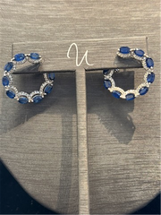 The Shappire and Diamond Wrap Around Hoops by Ryan Gems feature alternating blue sapphires and diamonds in 14k white gold, displayed on a gray jewelry stand.