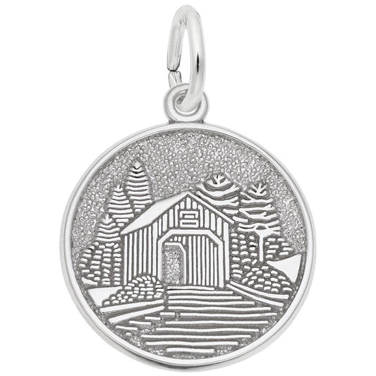 The Covered Bridge Disc Charm in Sterling Silver by Rembrandt Charms features an engraved design of a covered bridge encircled by trees. The textured background emphasizes the intricate scene, reflecting the artistry typical of Rembrandt Charms.