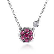 The 925 Sterling Silver Ruby Cluster And Diamond Pendant Necklace *Lusso from Gabriel & Co, part of the Lusso Color Collection, showcases a round pendant that features a central red gemstone encircled by six smaller red gemstones arranged in a floral pattern. The delicate chain also includes a smaller setting with a single clear gemstone.
