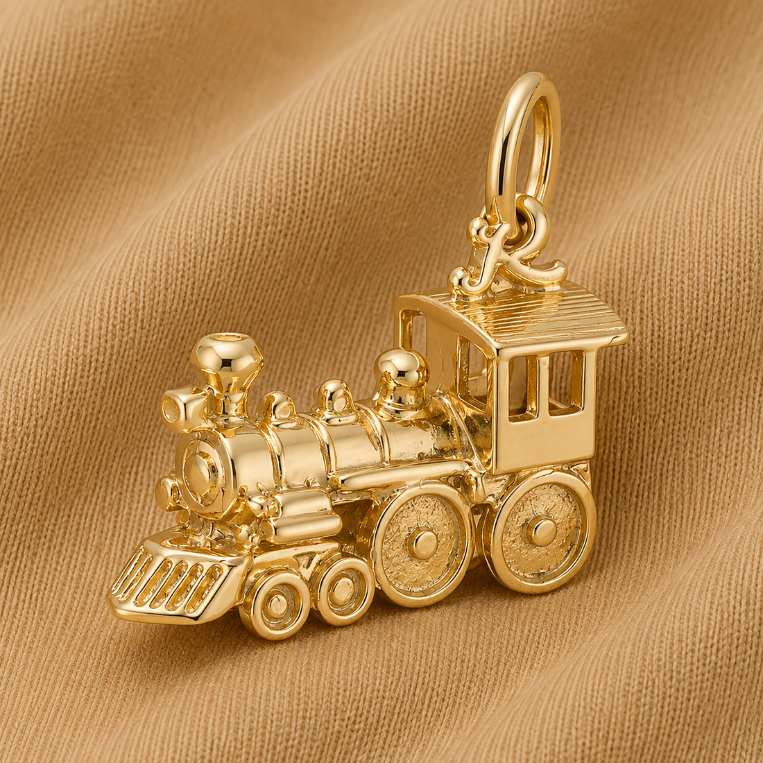 The Rembrandt Charms Train Engine Charm – Gold Plated is displayed on a soft, tan fabric background, making it an ideal piece of locomotive jewelry for collectors and train enthusiasts.