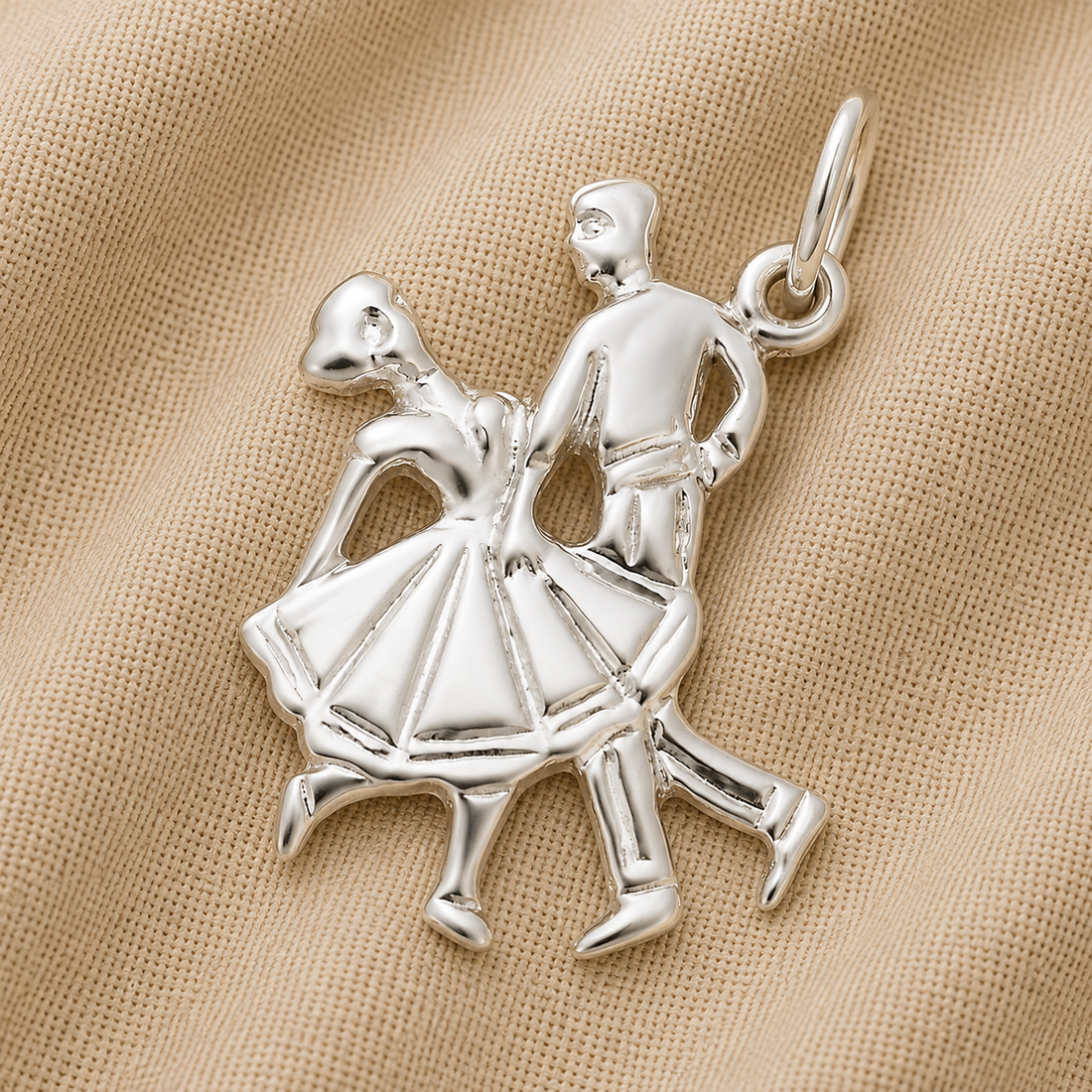 A beautiful Dancing Couple Charm in sterling silver from Rembrandt Charms, shaped like two dancers in mid-step and displayed on beige textured fabric—perfect for adding to your charm bracelet.