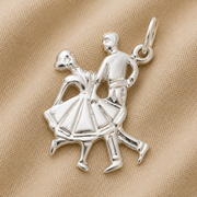 A beautiful Dancing Couple Charm in sterling silver from Rembrandt Charms, shaped like two dancers in mid-step and displayed on beige textured fabric—perfect for adding to your charm bracelet.