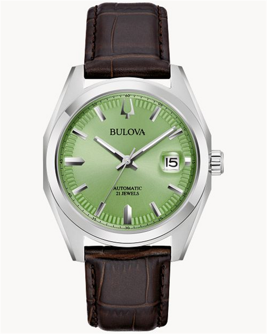 The Survey M Y ST GN Auto by Bulova Watch Company is a silver wristwatch featuring a light green dial, silver hour markers, and a date display at the 3 o'clock position. It boasts an automatic 21 jewels movement and is paired with a dark brown leather strap.