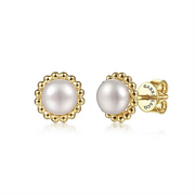 The pair of 14K Yellow Gold Bujukan Pearl Stud Earrings by Gabriel & Co features round white pearls at the center, elegantly encircled by delicate gold bead accents. The back of one earring is visible, showcasing the gold clasp engraved with the brand name.
