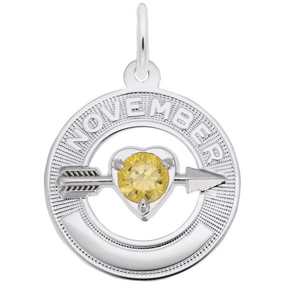 A round silver pendant features a citrine birthstone at the center of a heart pierced by an arrow. The word "NOVEMBER" is engraved at the top, signifying the birthstone for that month. This elegant piece, also known as the November Love Birthstone Charm / Sterling Silver by Rembrandt Charms, is perfect for any jewelry collection.