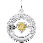 A round silver pendant features a citrine birthstone at the center of a heart pierced by an arrow. The word "NOVEMBER" is engraved at the top, signifying the birthstone for that month. This elegant piece, also known as the November Love Birthstone Charm / Sterling Silver by Rembrandt Charms, is perfect for any jewelry collection.