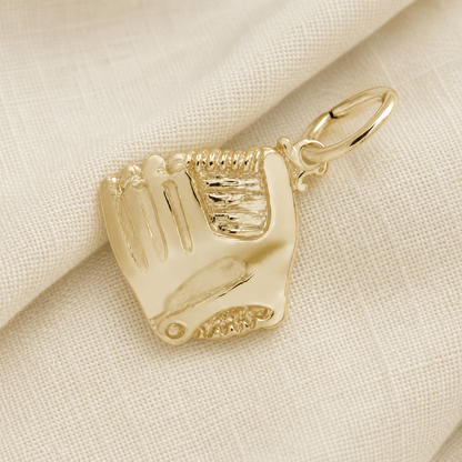 A gold-plated “Baseball Glove with Ball Charm” by Rembrandt Charms rests on a textured, off-white fabric background. This charm showcases detailed stitching on the glove and includes a small loop for attaching to a chain, making it an ideal piece of baseball jewelry or a treasured keepsake for any fan.