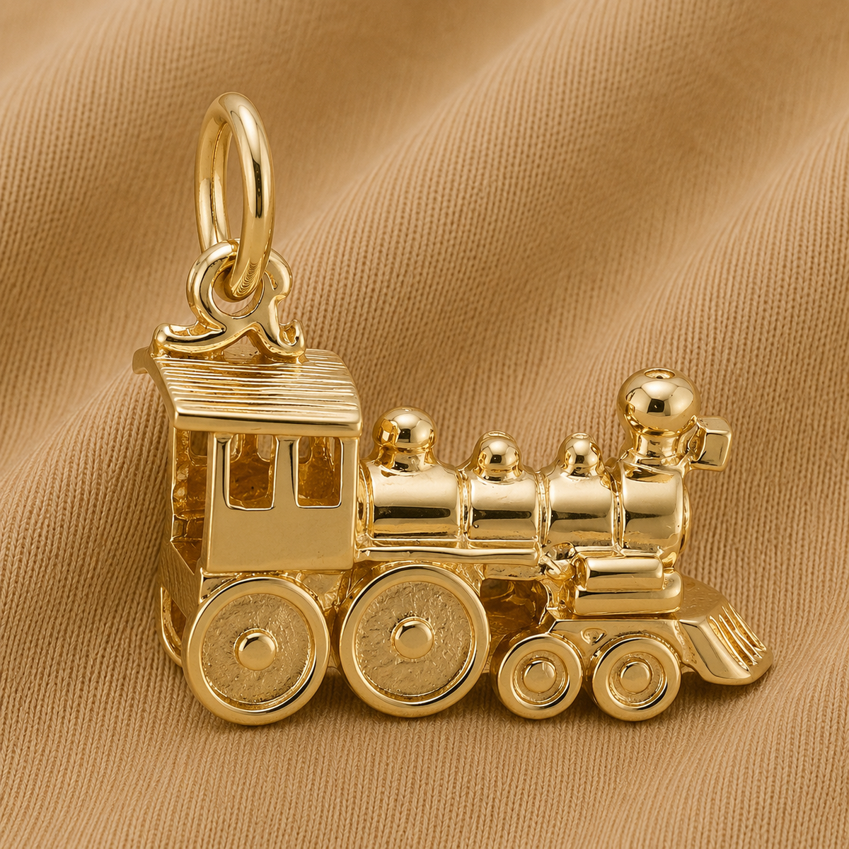 The Rembrandt Charms Train Engine Charm- Gold Plated, featuring detailed wheels and smoke stacks, is the perfect accessory for locomotive jewelry enthusiasts and is displayed here on a soft tan fabric background.
