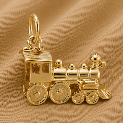 The Rembrandt Charms Train Engine Charm- Gold Plated, featuring detailed wheels and smoke stacks, is the perfect accessory for locomotive jewelry enthusiasts and is displayed here on a soft tan fabric background.