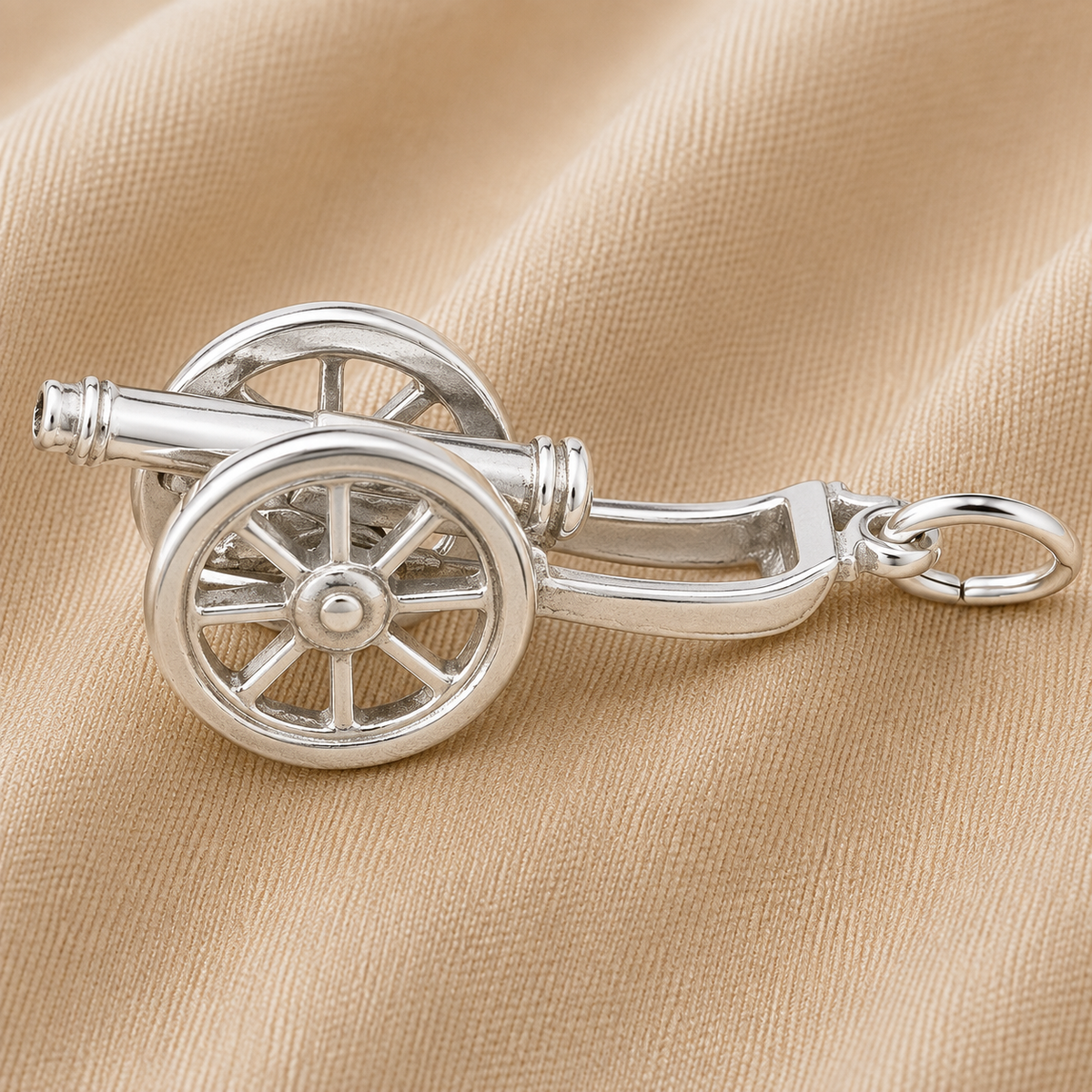 The Cannon Charm - Sterling Silver by Rembrandt Charms, featuring detailed wheels that evoke a sense of military heritage, is showcased against a beige, textured fabric background.