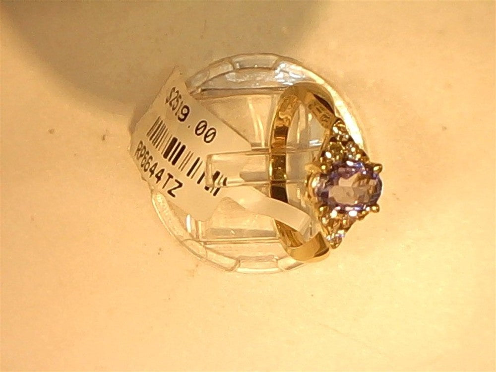 A Ryan Gems Oval Tanzanite and Diamond ring in 14k yellow gold, size 7, featuring a purple center stone with diamond accents, is displayed on a clear stand with a $219.00 price tag and barcode attached.