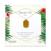A gold necklace with a rectangular pendant featuring the Protect Me Hamsa symbol, from Dogeared's "Protect Me Hamsa / GP-SS" collection, is displayed on a card adorned with green geometric and floral designs. The card includes the words "Protect Me" and "Wear your necklace as a reminder that all will be well," along with product details like GP-SS.