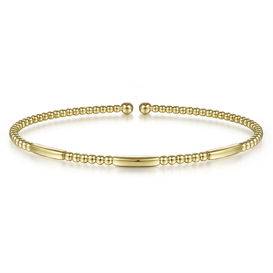 This 14K Yellow Gold Bujukan Open Bangle from Gabriel & Co features a slim, open design with small round gold beads alternating with smooth, elongated gold bars. The ends are capped with slightly larger round beads, and it boasts a shiny, polished finish.