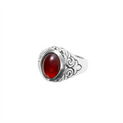The King Baby Garnet Oval Stone Ring W/ Wing Detail features ornate floral engravings, wing accents, and a large oval red garnet at its center, shown against a plain white background.