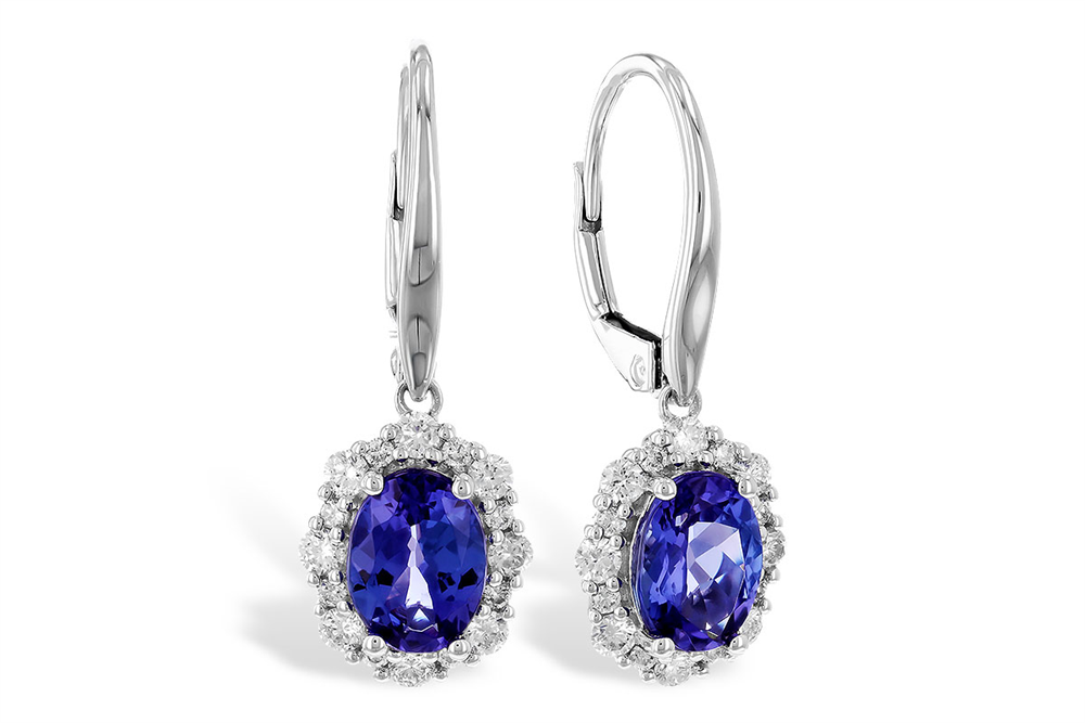 This image displays a pair of elegant drop earrings featuring vibrant oval-cut blue gemstones, surrounded by a halo of small white diamonds. The deep blue stones are set in a white metal frame, enhancing their color and brilliance. The earrings have lever-back clasps, adding a secure and sophisticated touch to this classic design.