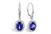 This image displays a pair of elegant drop earrings featuring vibrant oval-cut blue gemstones, surrounded by a halo of small white diamonds. The deep blue stones are set in a white metal frame, enhancing their color and brilliance. The earrings have lever-back clasps, adding a secure and sophisticated touch to this classic design.