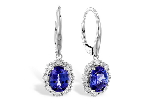 This image displays a pair of elegant drop earrings featuring vibrant oval-cut blue gemstones, surrounded by a halo of small white diamonds. The deep blue stones are set in a white metal frame, enhancing their color and brilliance. The earrings have lever-back clasps, adding a secure and sophisticated touch to this classic design.