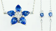 A close-up image of the exquisite Bellarri Sapphire and Diamond Necklace D-0.15 SAPP-2.00. The pendant, crafted in the shape of a flower, showcases five stunning blue sapphire petals surrounding a cluster of small diamonds. The delicate chain is embellished with two additional small sapphires set in circular frames, enhancing this breathtaking piece of jewelry.