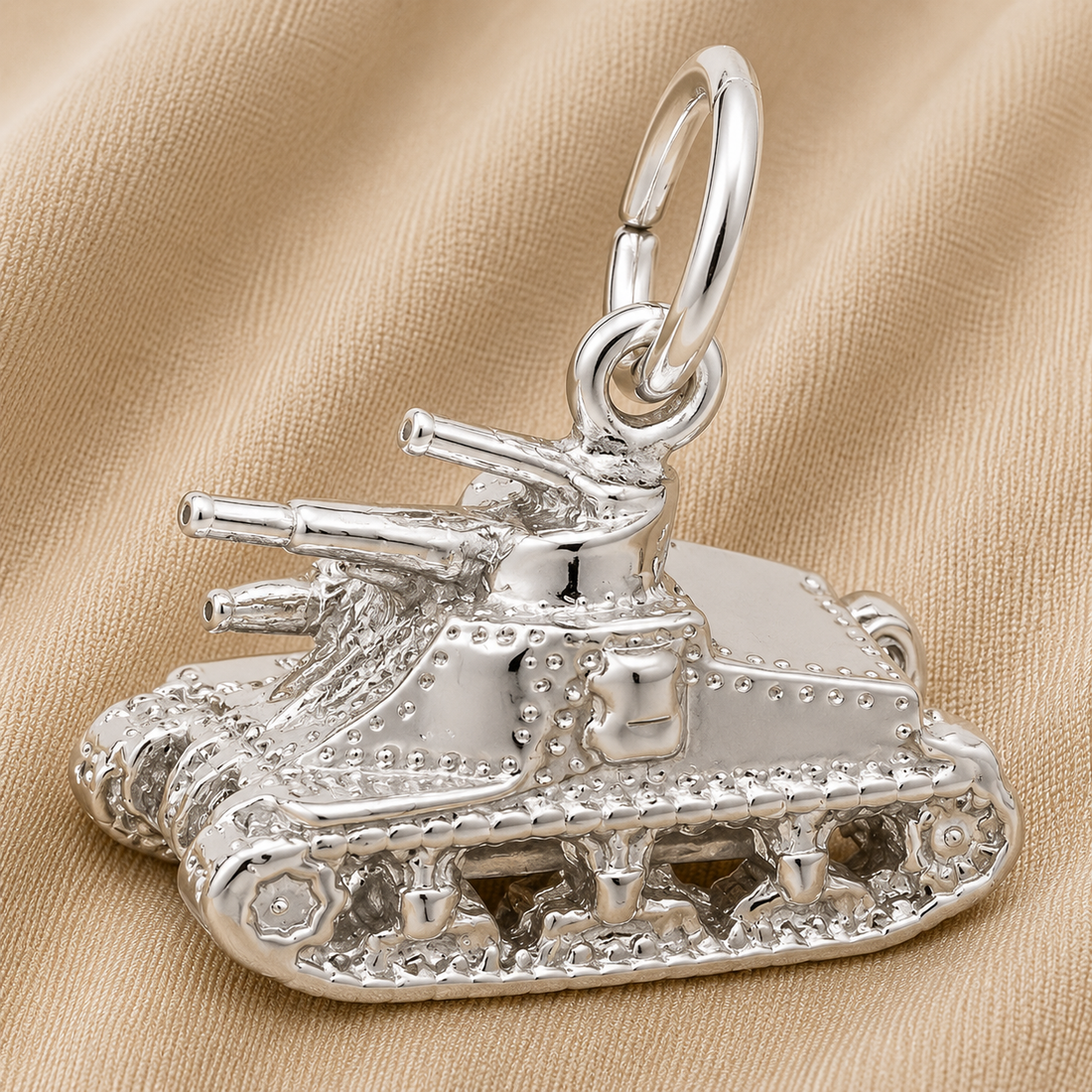 A gleaming Sterling Silver Tank Charm by Rembrandt Charms, complete with intricate treads and cannons, rests on beige fabric. This eye-catching piece of military jewelry includes a convenient loop for easy attachment to a chain or bracelet, making it a meaningful gift for veterans or a treasured collector’s keepsake.