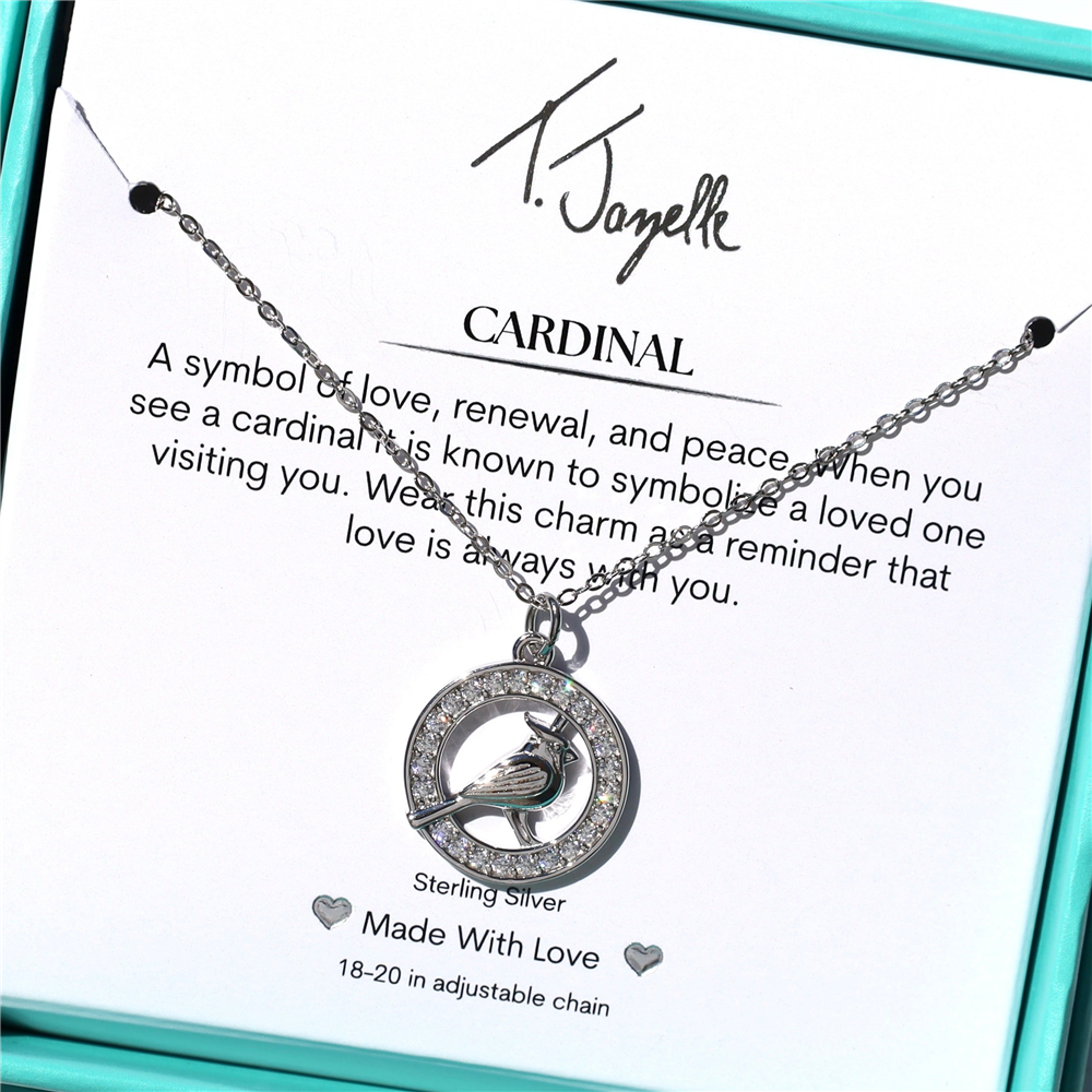 The T Jazelle Cardinal Sterling necklace features a White Cardinal CZ sterling silver charm, displayed in a turquoise box with a card describing the cardinal as a symbol of love, renewal, and peace.