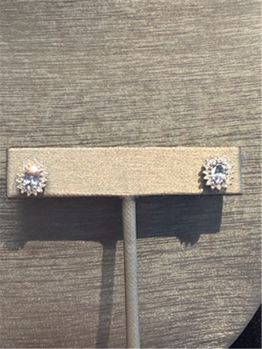 A pair of Ryan Gems Tanzanite with Diamond Halo Studs in 14k white gold, featuring tanzanite centers surrounded by sparkling diamonds, displayed on a beige stand against a neutral background.