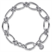 The Gabriel & Co Sterling Silver Bujukan Link Bracelet | 7" features large, elongated oval links intricately connected by smaller decorative elements. A small circular charm with an engraved design hangs near the clasp, adding a unique touch. This exquisite piece, part of the Bujukan Collection, is crafted in 925 silver.