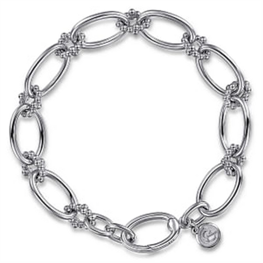 The Gabriel & Co Sterling Silver Bujukan Link Bracelet | 7" features large, elongated oval links intricately connected by smaller decorative elements. A small circular charm with an engraved design hangs near the clasp, adding a unique touch. This exquisite piece, part of the Bujukan Collection, is crafted in 925 silver.