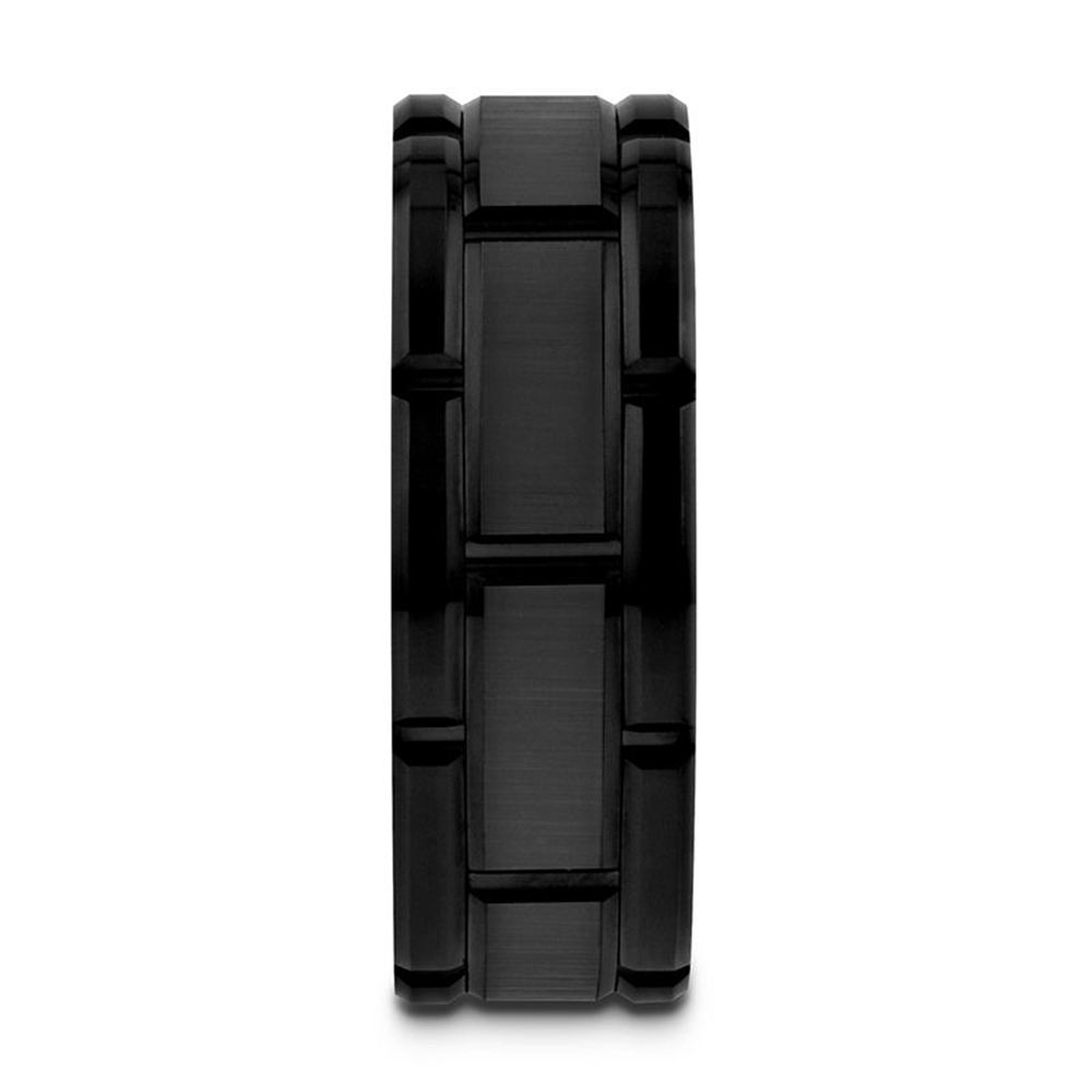 The WINDSOR Beveled Black Tungsten Carbide Wedding Band by Thorsten features a segmented, block-like design. This ring has a matte finish with slightly raised, glossy interlocking segments that give it a rugged, industrial appearance. The white background makes this black tungsten carbide band the central focus.