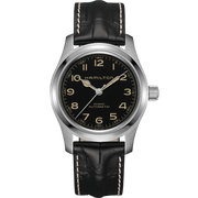 A KHAKI FIELD MECH GN NATO H50 / ZYH5Y4N62 Hamilton watch with a black dial featuring Arabic numerals and a date display at the 3 o'clock position. The watch has a silver stainless steel case and a black leather strap with white stitching, embodying rugged elegance distinctly present in every detail.