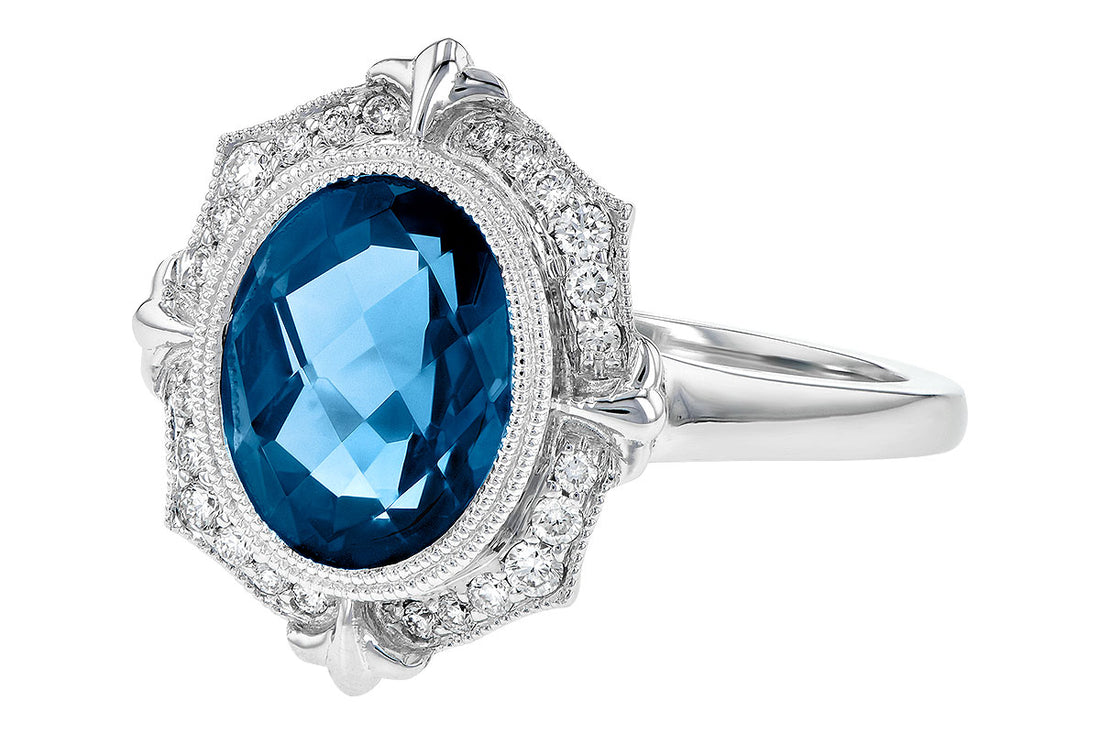 The Allison Kaufman London Blue Topaz and Diamonds 14k White Gold Ring showcases a striking oval London blue topaz at its center, elegantly surrounded by intricate white gold detailing with small diamonds, all crafted in an ornate, vintage-inspired design.
