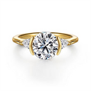 The Gabriel & Co 14K Yellow Gold Half Bezel Round Three Stone Diamond Engagement Ring features a large center diamond and two side stones, beautifully displayed on a white background.