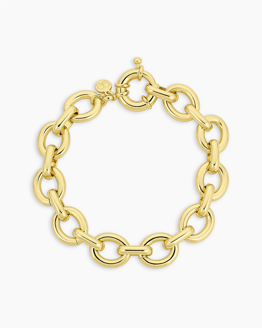 The Gorjana Adriana Bracelet features thick round 18k gold-plated links and a toggle clasp, displayed in a circular shape on a plain white background.