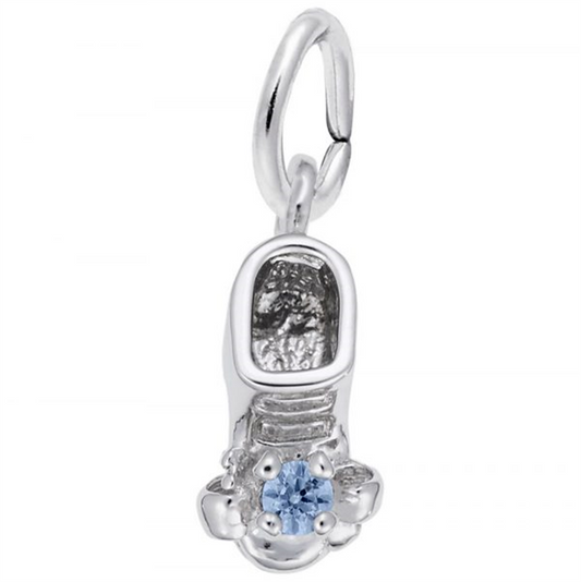 The December Baby Bootie Charm by Rembrandt Charms is a sterling silver pendant shaped like a sneaker, featuring intricate details such as shoelaces and tread. Adorned with a small blue gemstone at the center, the charm includes a ring at the top for easy attachment to a chain or bracelet.