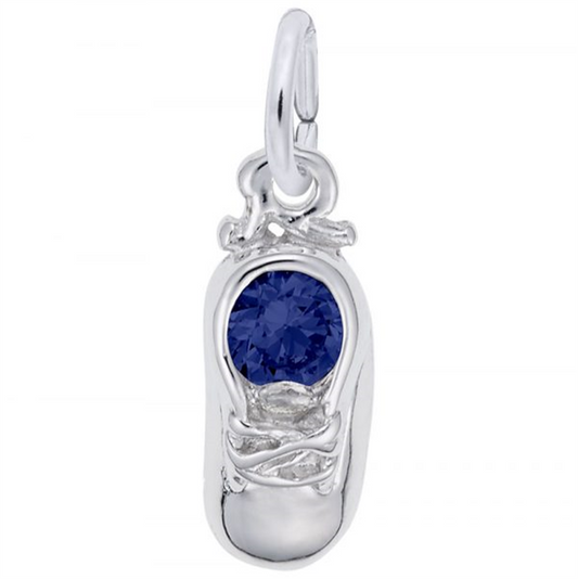 The Rembrandt Charms baby shoe pendant, crafted from sterling silver, features a round blue gemstone at its center with intricate laces and a loop for easy attachment to a chain.